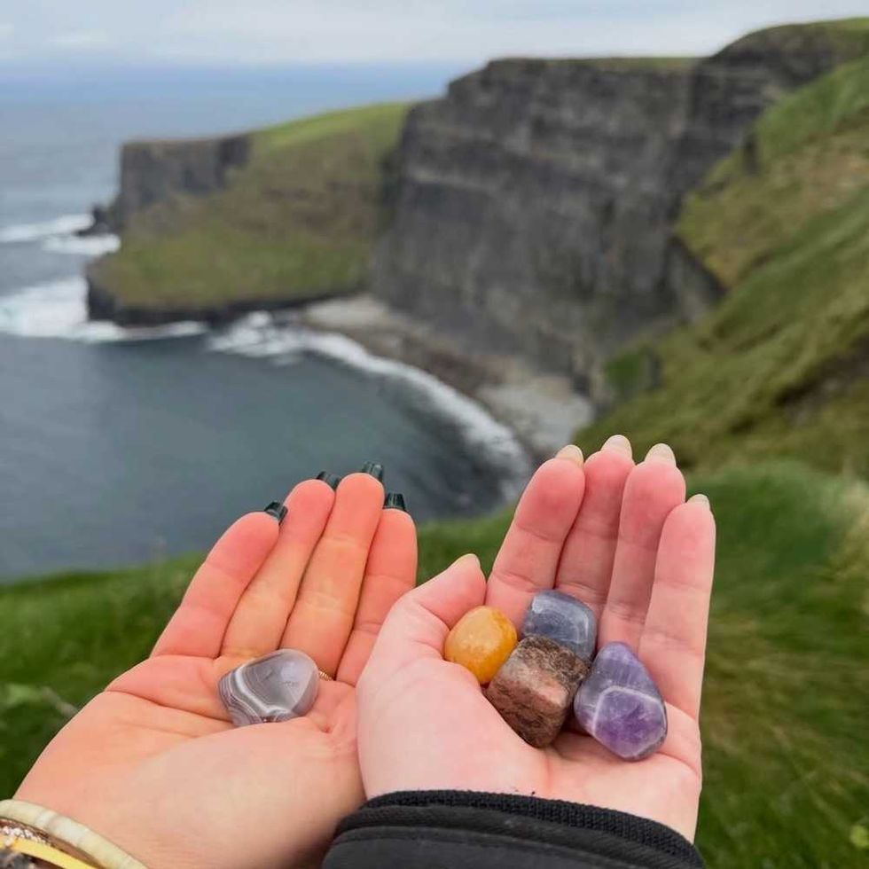 Hands holding colorful stones with cliffs and sea in the background.
