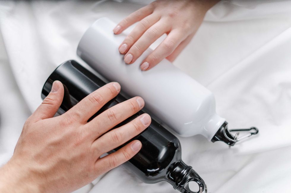 Hands touching black and white water bottles on a white surface.