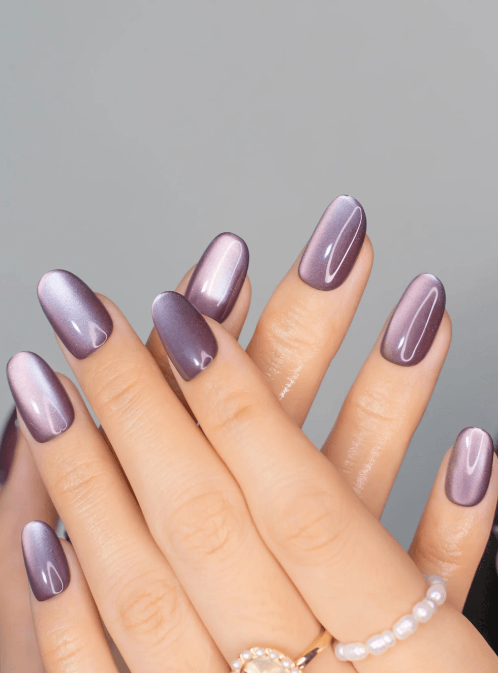 Hands with glossy purple nail polish and a pearl ring on one finger.