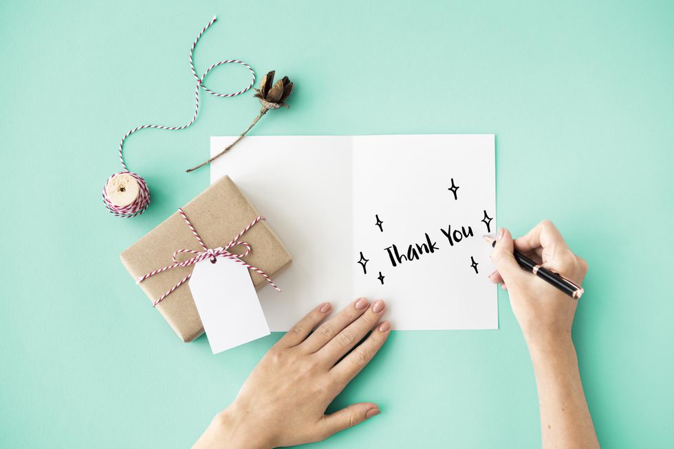 Handwriting "Thank You" on a card next to a wrapped gift on a mint background.