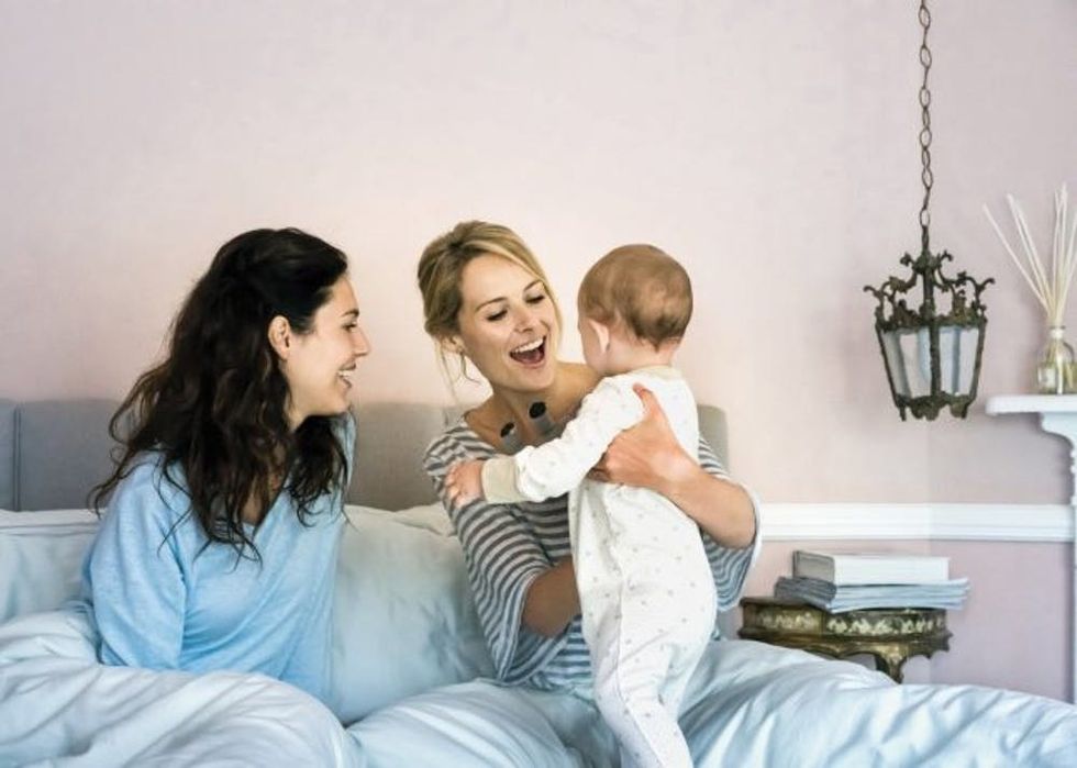 Happy young lesbians playing with baby boy in bed