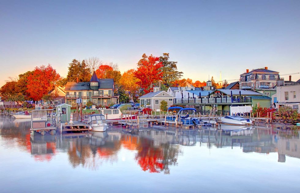 Harbor scene with boats, colorful autumn trees, and charming houses reflecting on the water.