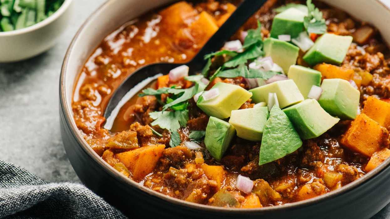 Hearty chili with avocado, cilantro, and diced onions in a bowl with a spoon.