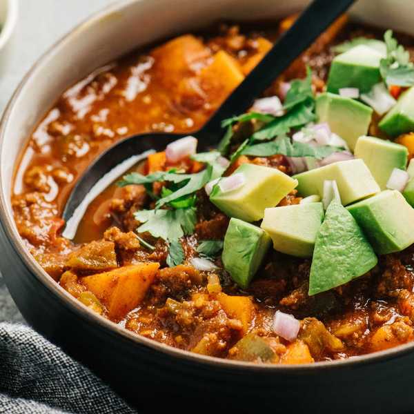 Hearty chili with avocado, cilantro, and diced onions in a bowl with a spoon.