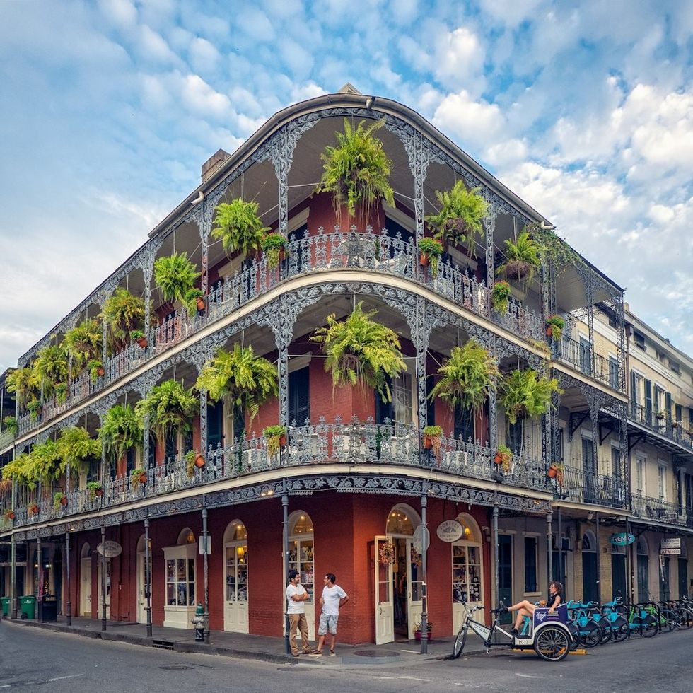 Historic building with ornate ironwork balconies and hanging plants on a corner in New Orleans.