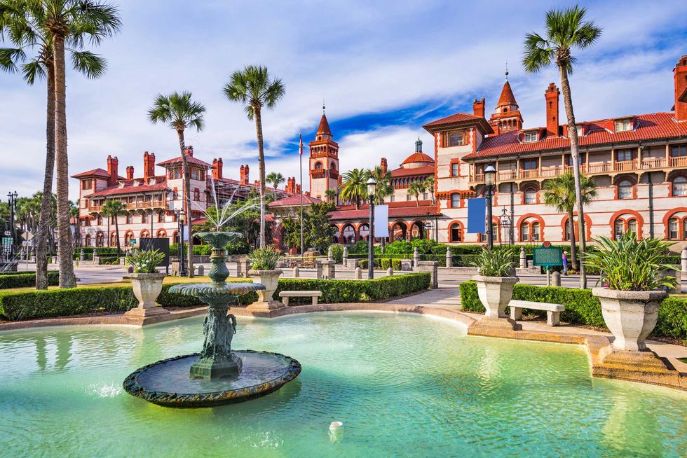 Historic building with red roofs, palm trees, and a fountain in the foreground.