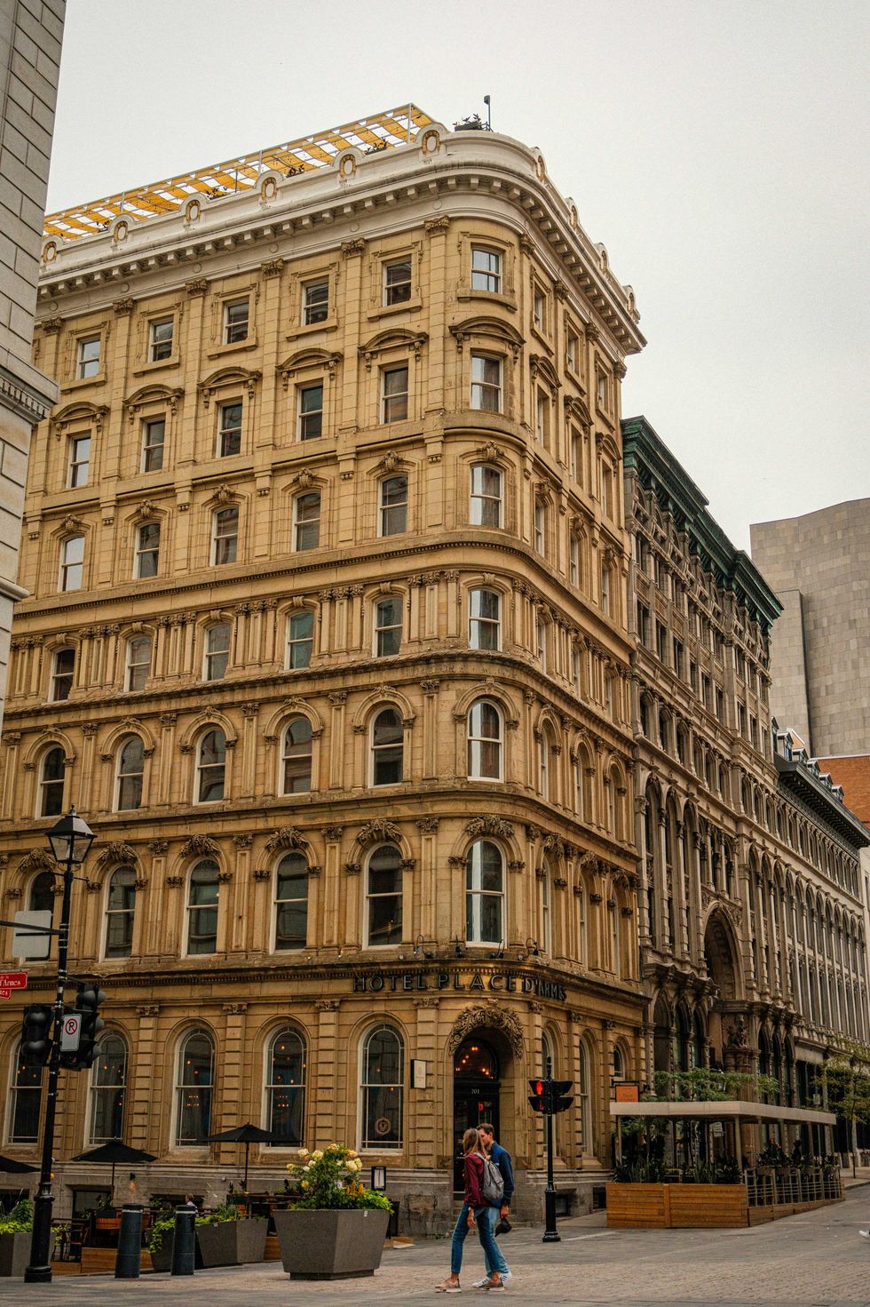 Historic corner building with ornate architecture, pedestrians walking below, overcast sky.