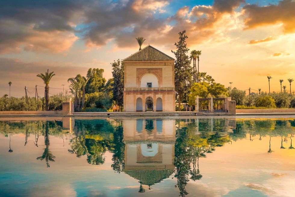 Historic pavilion by a reflective pool, surrounded by trees at sunset.