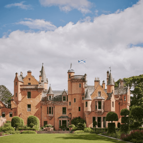 Historic Scottish castle with turrets and a flag, surrounded by lush gardens under a cloudy sky.