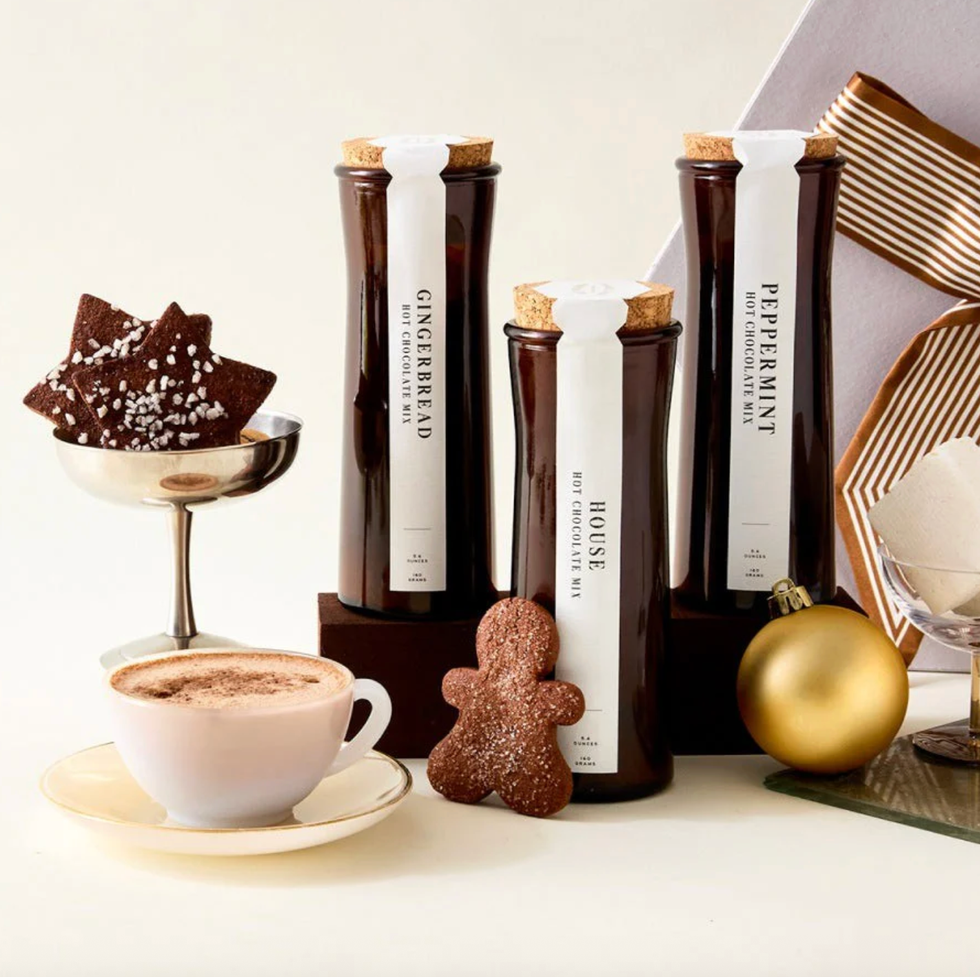 Hot chocolate mixes with a cup, gingerbread, and star cookies, plus gold ornaments.