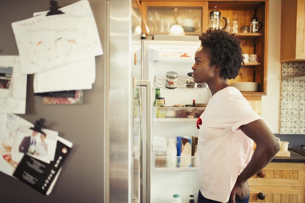 Hungry woman peering into refrigerator in kitchen