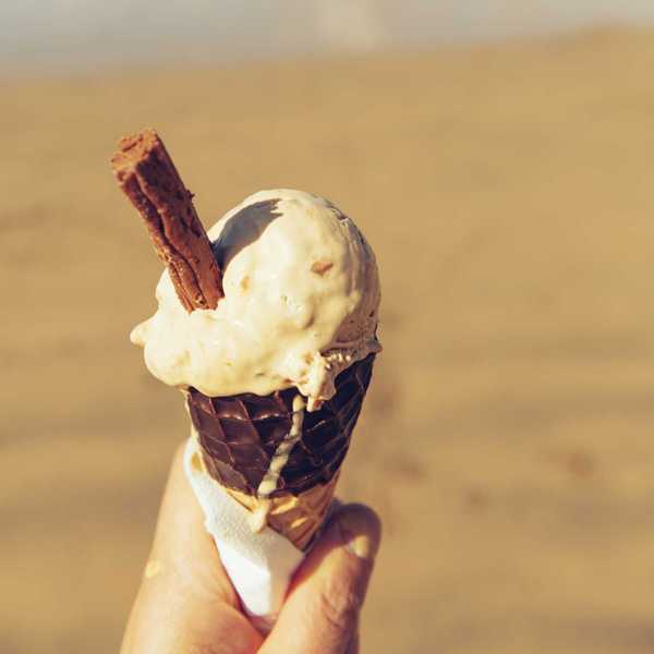 Ice cream cone with a chocolate stick held in hand, beach in background.