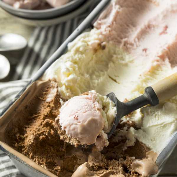 Ice cream scoop in a tub with chocolate, vanilla, and strawberry flavors.