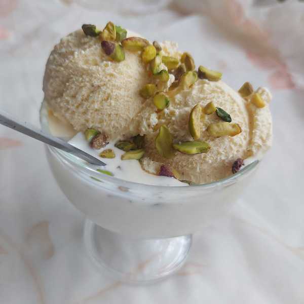 Ice cream topped with pistachios in a glass bowl, with a spoon on the side.