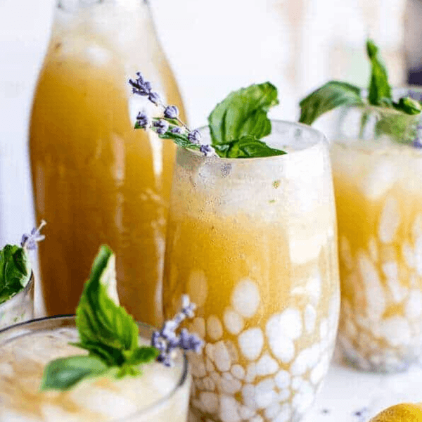 Icy lavender lemon cocktails with mint and lemon garnish on a white surface.