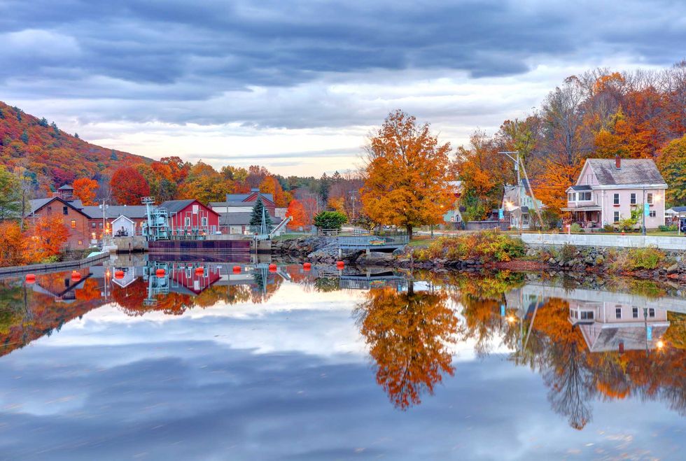 Idyllic autumn village scene with vibrant trees reflecting on a calm lake.