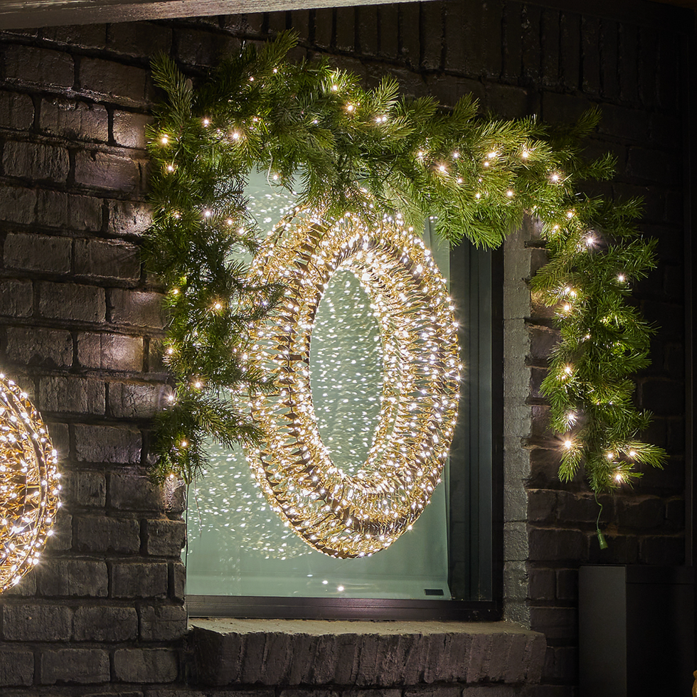 Illuminated wreath and garland with white lights on a brick wall window at night.
