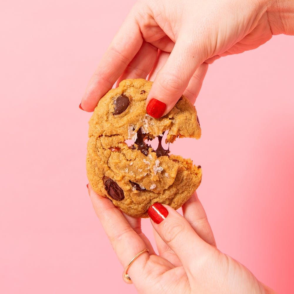 Chocolate chip cookie in hands with red nail polish being pulled apart