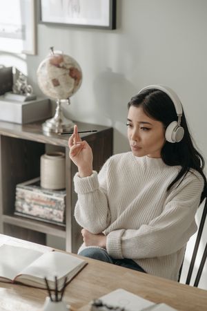 A woman is wearing headphones and has a pen in her hand. 