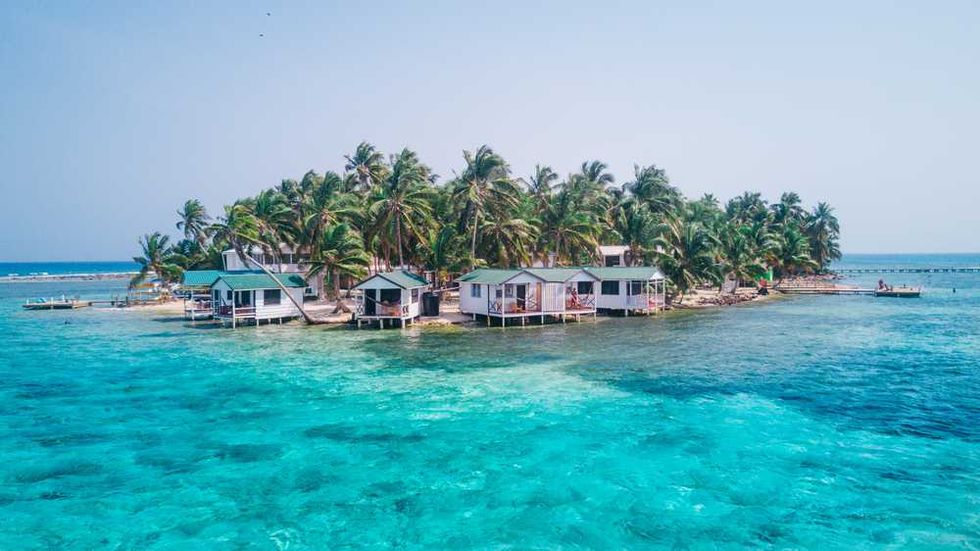 Island with palm trees and huts surrounded by turquoise ocean.