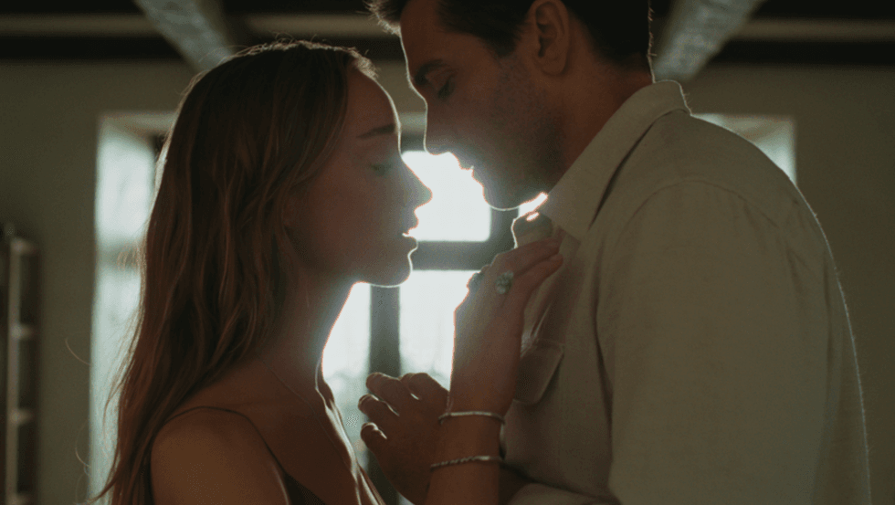 Jake Gyllenhaal and Phoebe Dynevor standing closely, backlit by sunlight through a window.