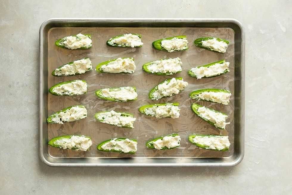 Jalape\u00f1o halves filled with cream cheese on a baking tray.