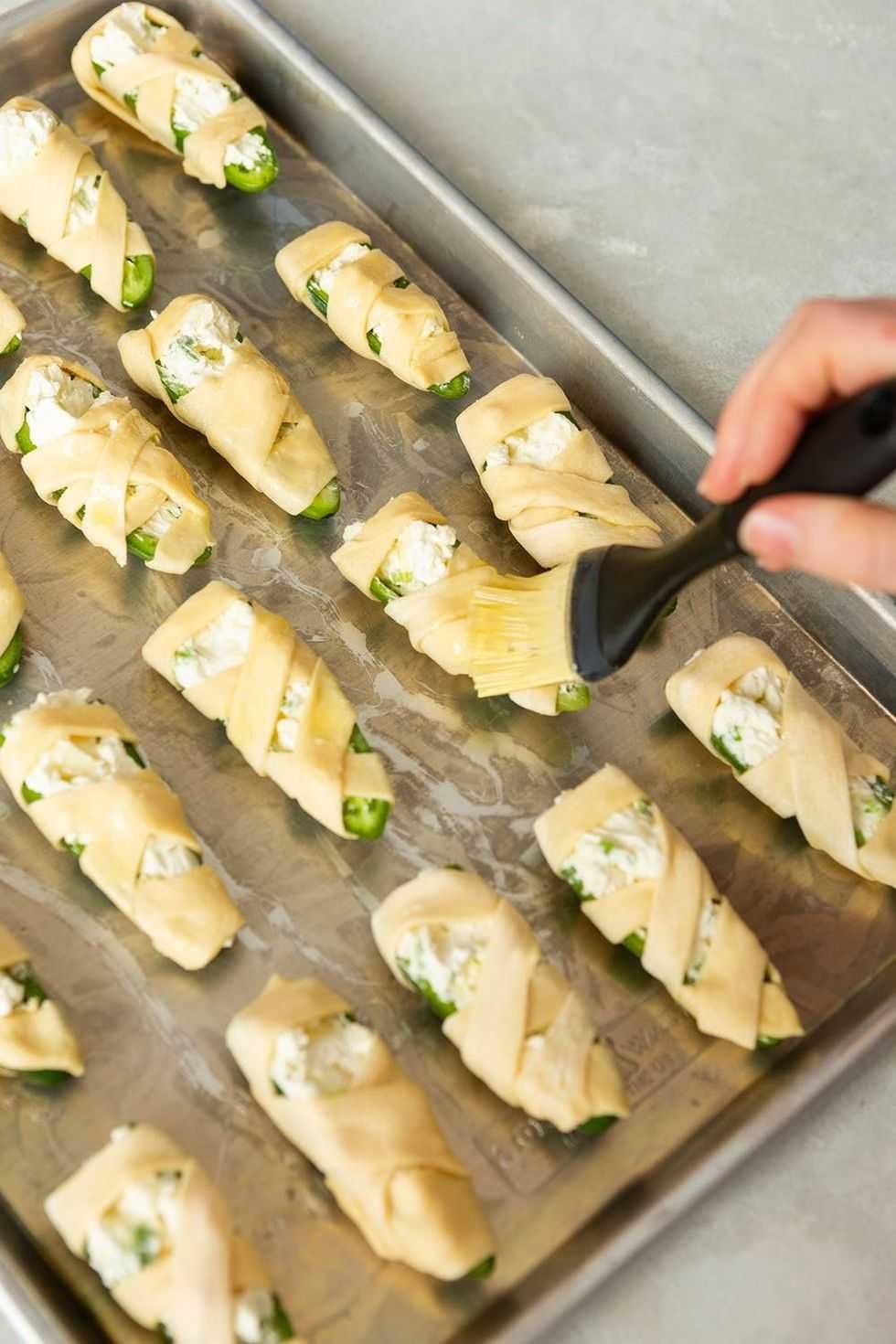 Jalape\u00f1os wrapped in dough on a baking tray, brushed with oil.