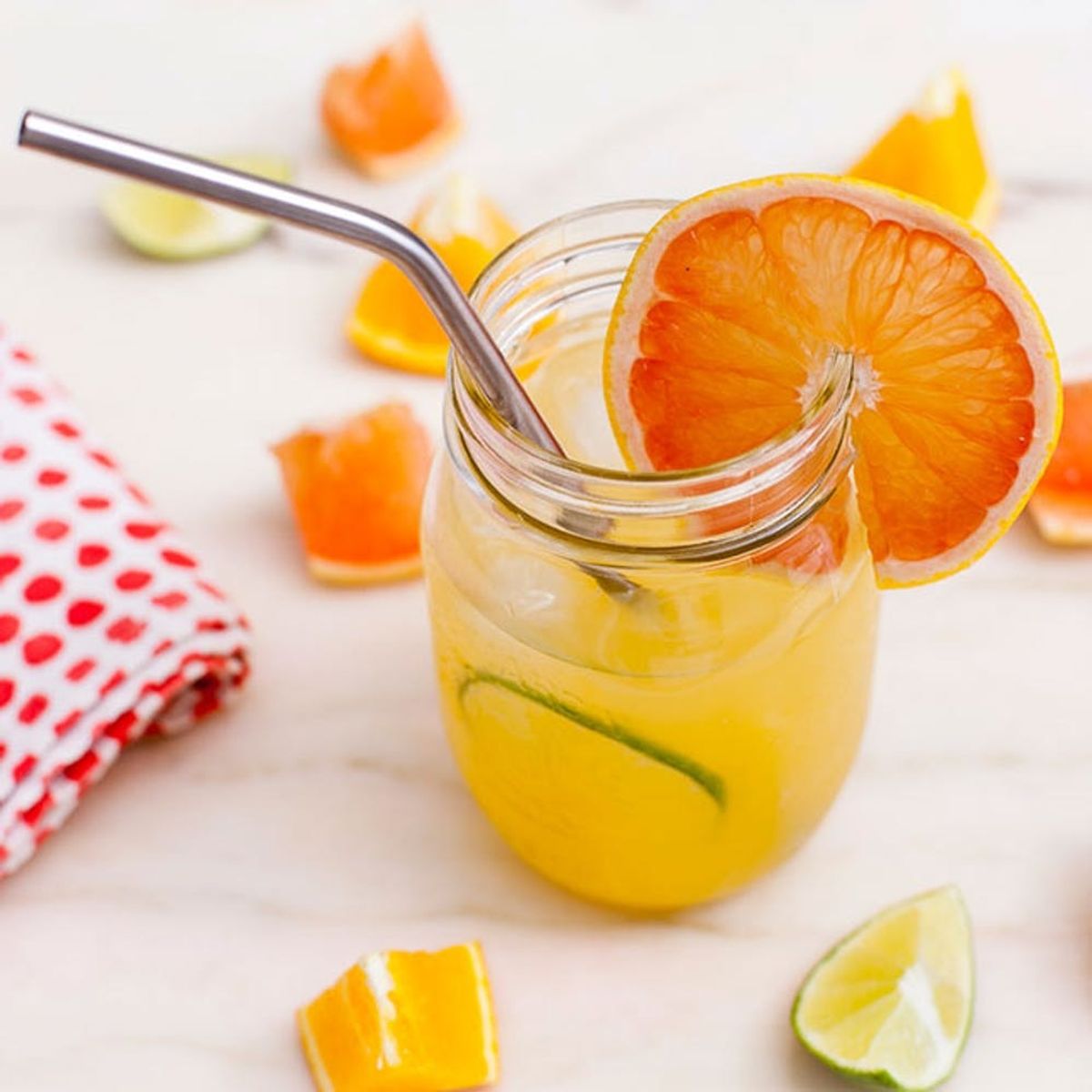 Jar of citrus juice with a metal straw, garnished with a slice of orange.