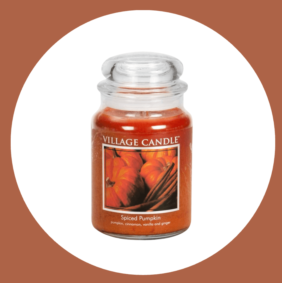 Jar of Village Candle spiced pumpkin scented candle, on a brown and white background.