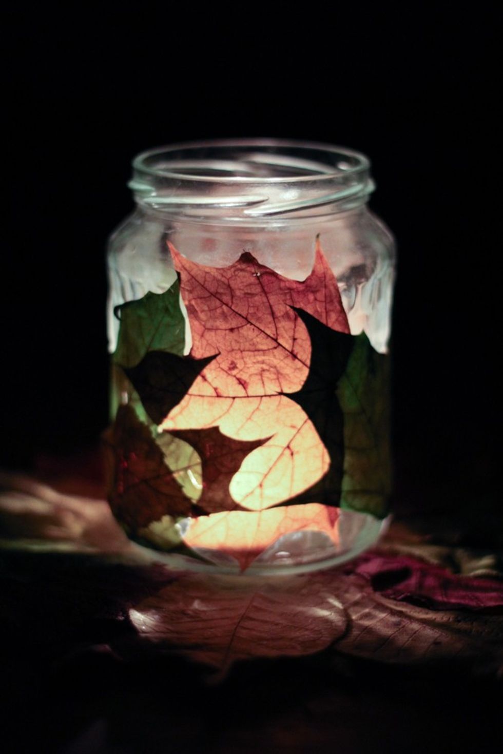 Jar with candle glow, decorated with autumn leaves in a dark setting.