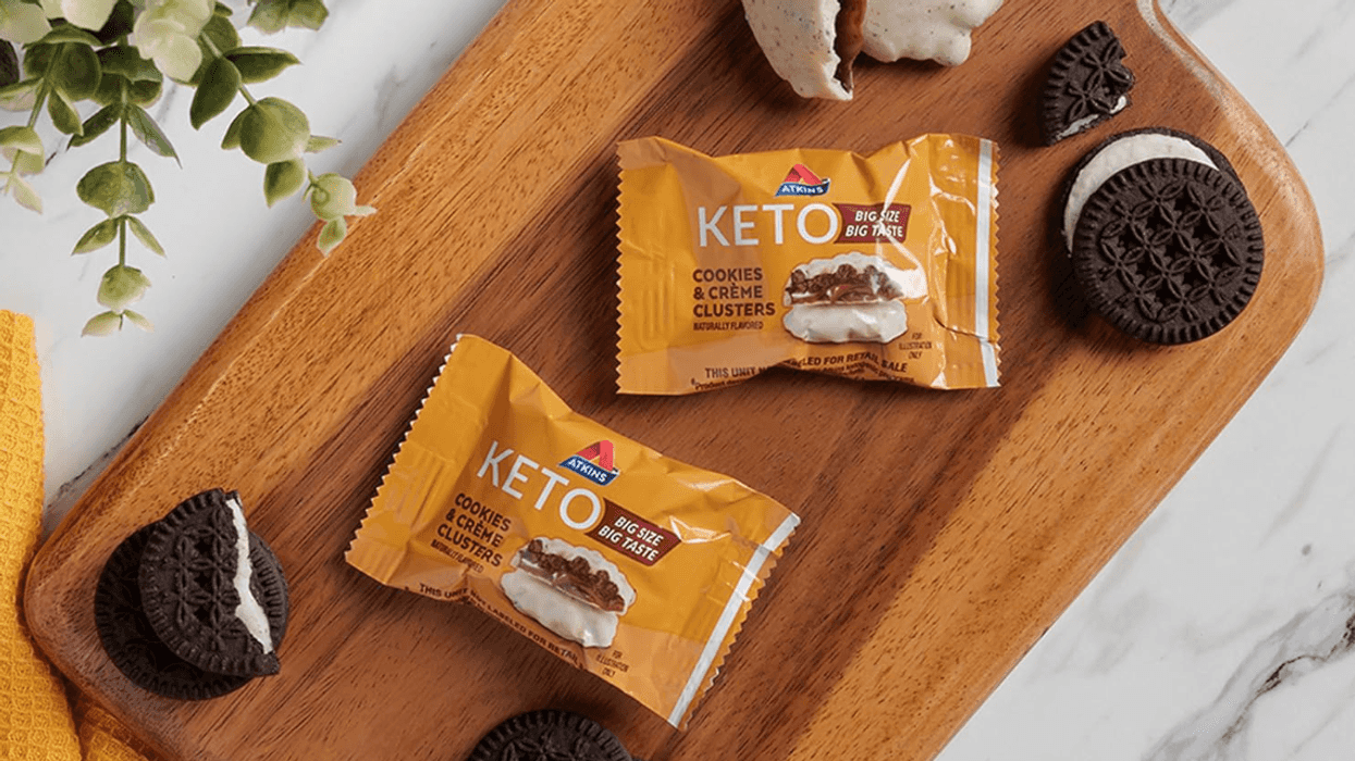 Keto cookie packs and cookies on a wooden board, near a plant and yellow cloth.
