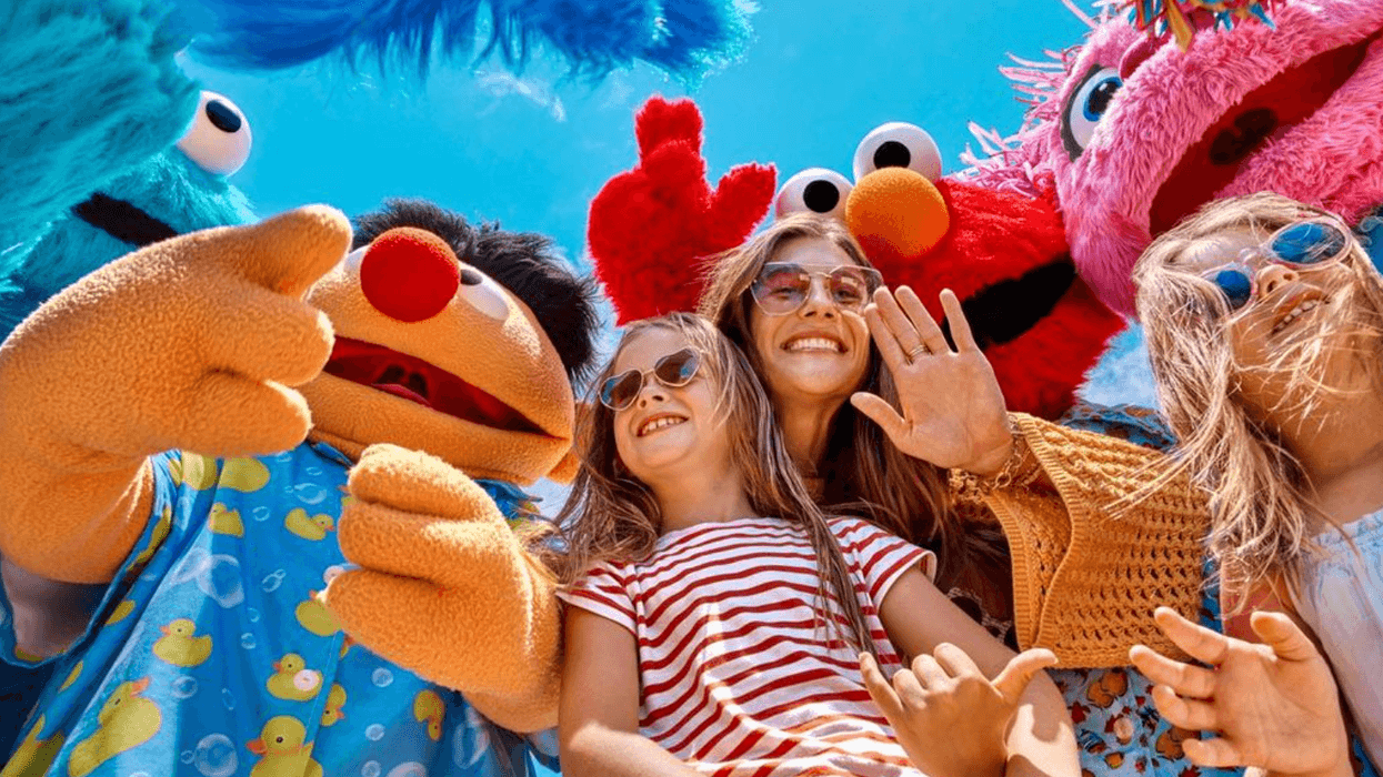 Kids and adults smiling with colorful mascots under a bright blue sky.