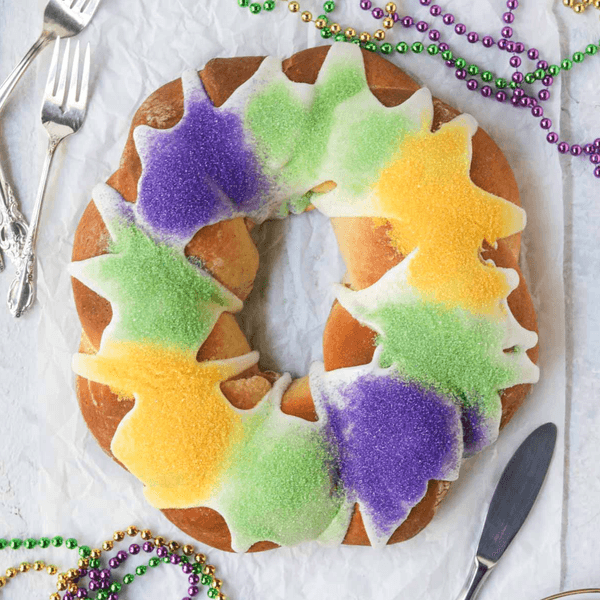 King cake with purple, green, and yellow sugar, surrounded by Mardi Gras beads.
