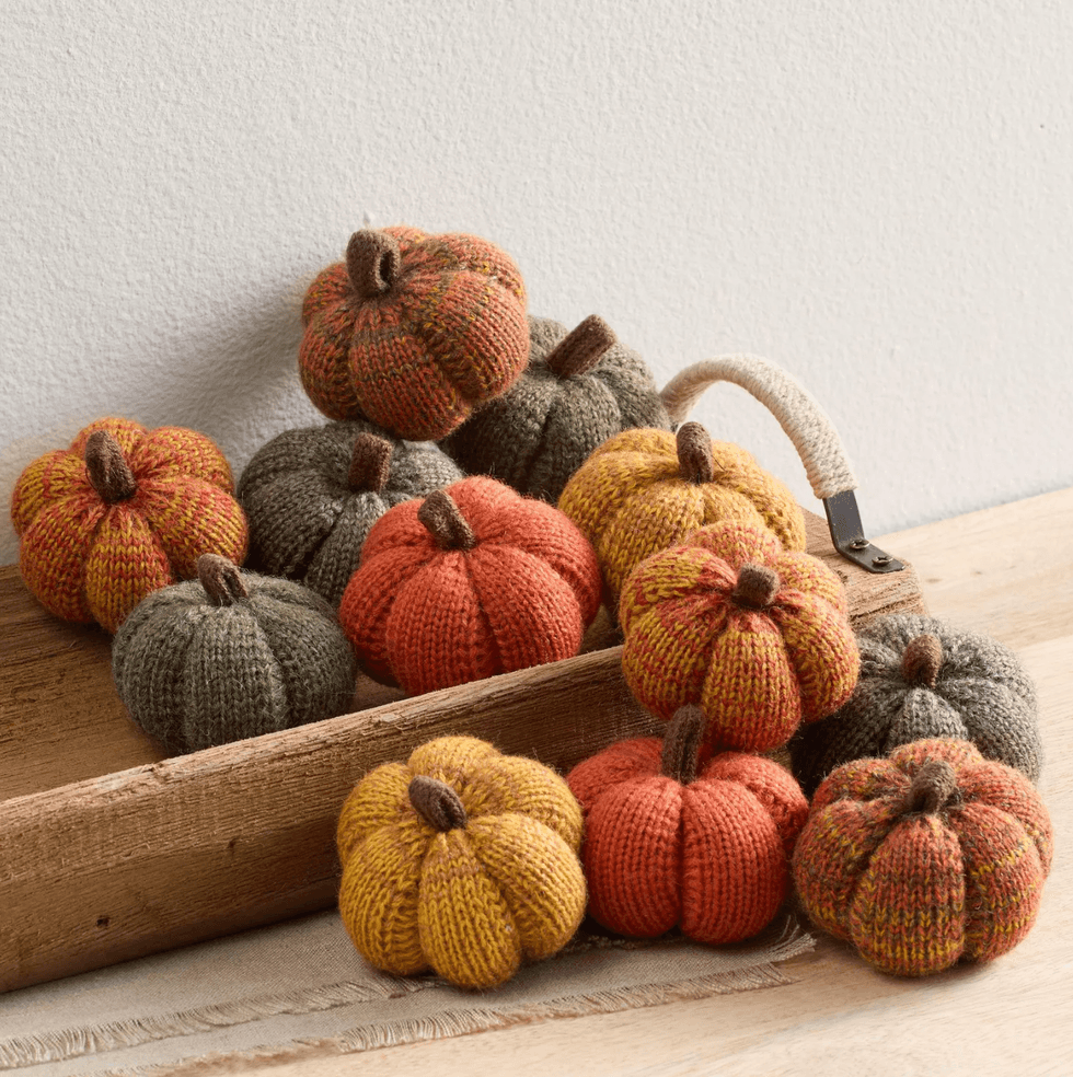 Knit pumpkins in autumn colors displayed in a rustic wooden tray.