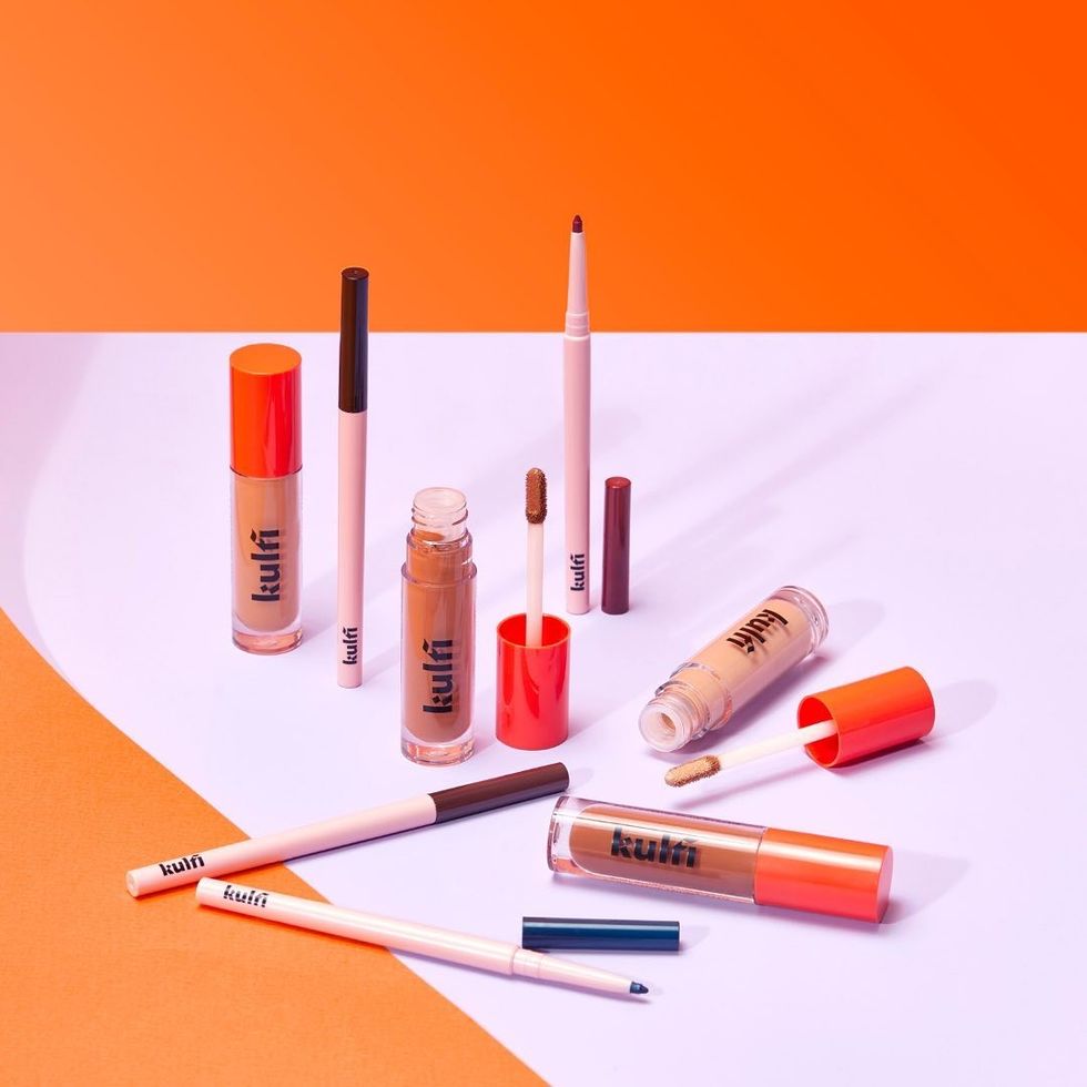Kulfi Beauty makeup products are sitting against an orange and purple background.