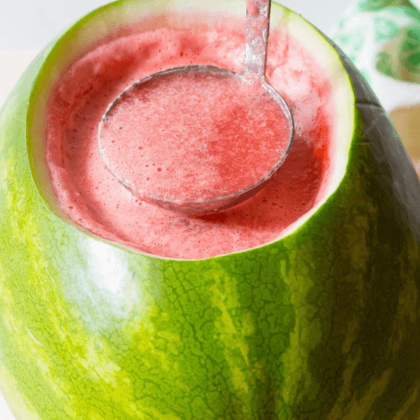 Ladle scooping pink drink from a carved watermelon container.