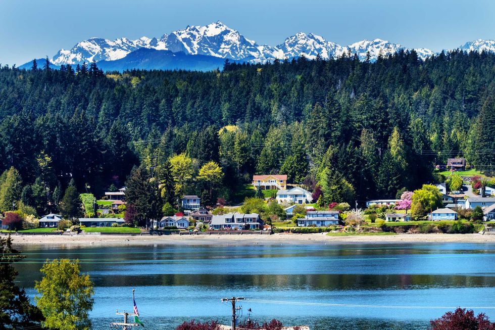Lakeside houses with snowy mountains and forests in the background.