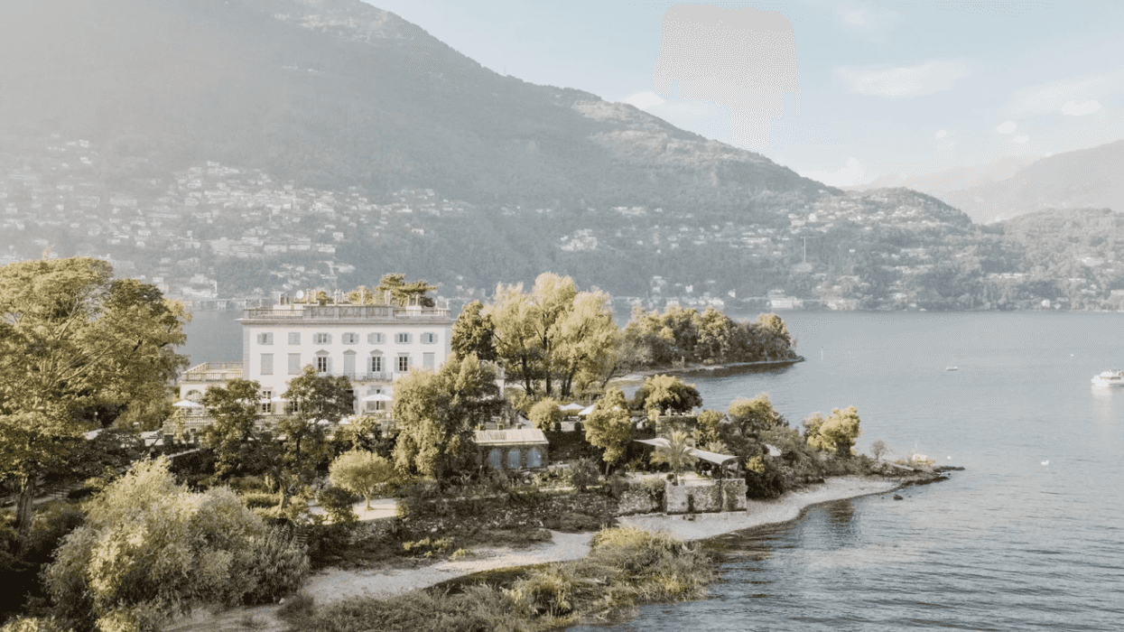 Lakeside villa surrounded by trees, with mountains in the background.