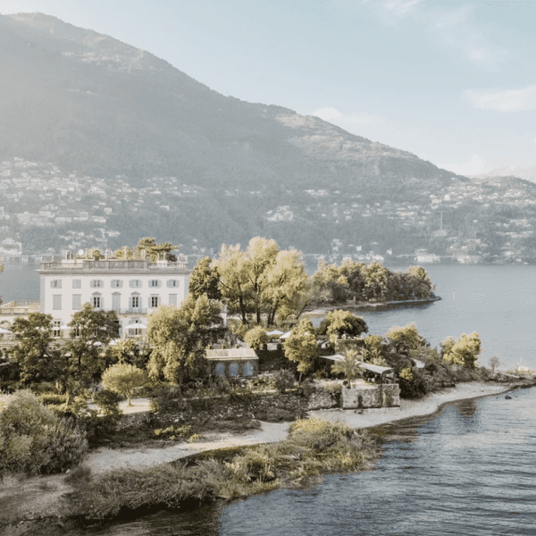 Lakeside villa surrounded by trees, with mountains in the background.