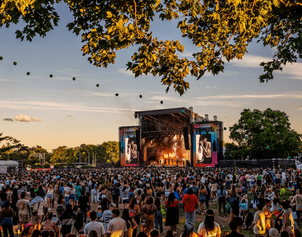 Large outdoor concert crowd watching a band on stage at sunset.