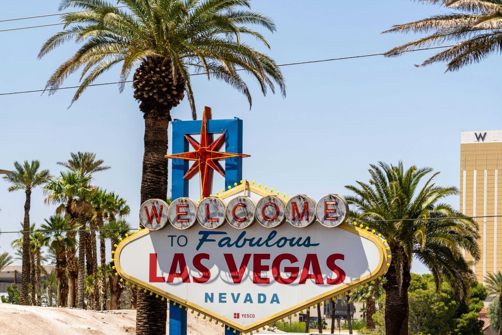 Las Vegas sign with palm trees and buildings in the background under a clear blue sky.