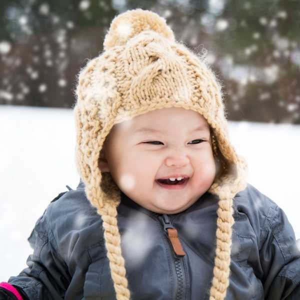 Laughing child in a snowstorm, wearing a knitted hat and coat.