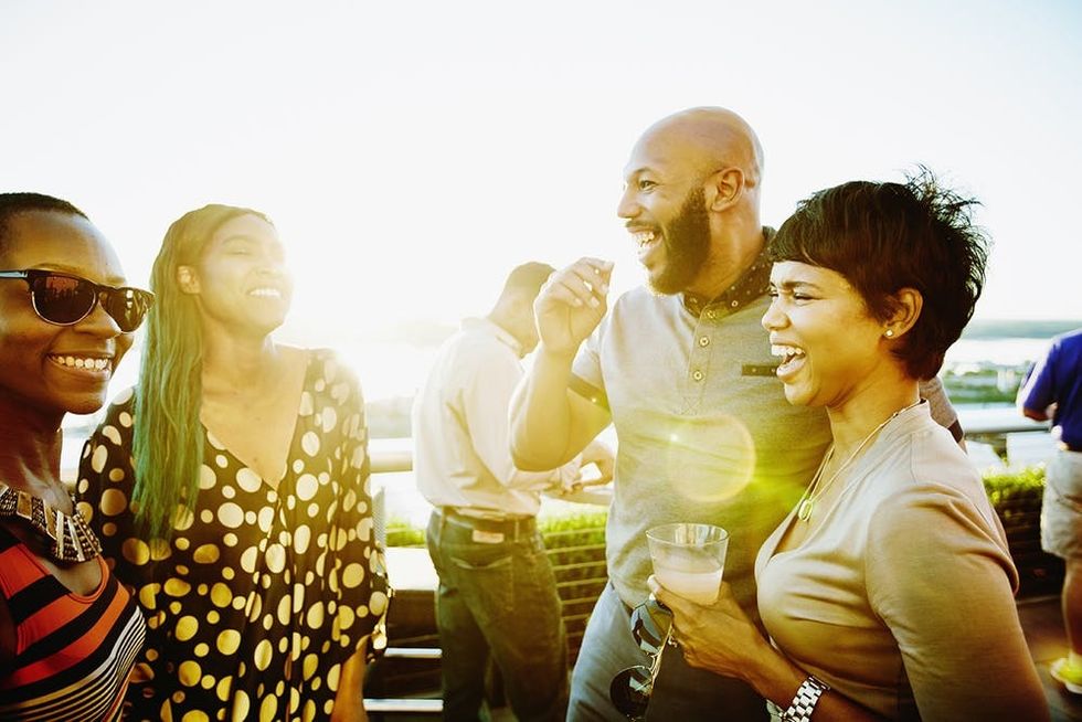Laughing couple sharing drinks with friends on rooftop restaurant deck on summer evening