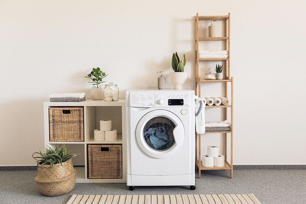 Laundry room with washing machine, shelves, baskets, plants, and stacked towels.
