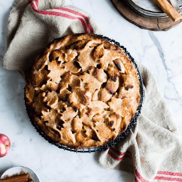 Leaf-patterned apple pie on a wire rack with a cloth on a marble surface.