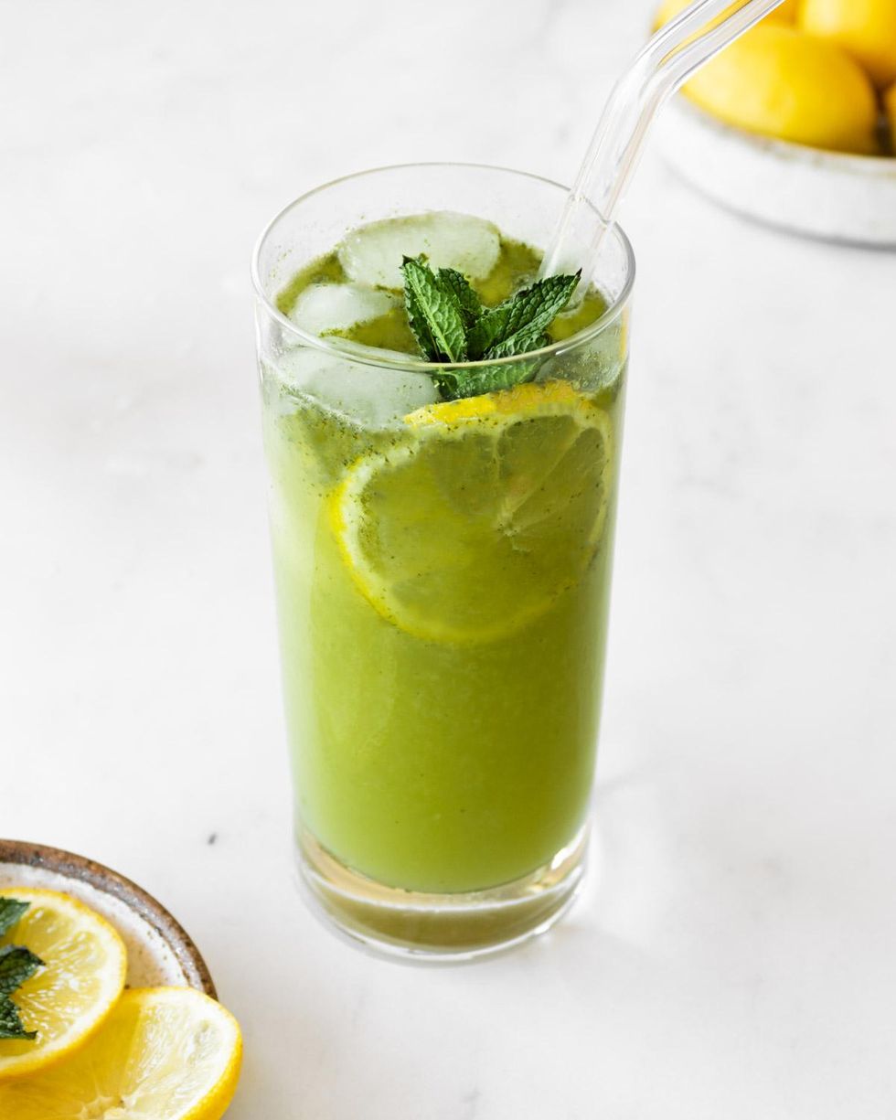 Lebanese mint lemonade with a straw and garnished with a lemon slice and mint leaf
