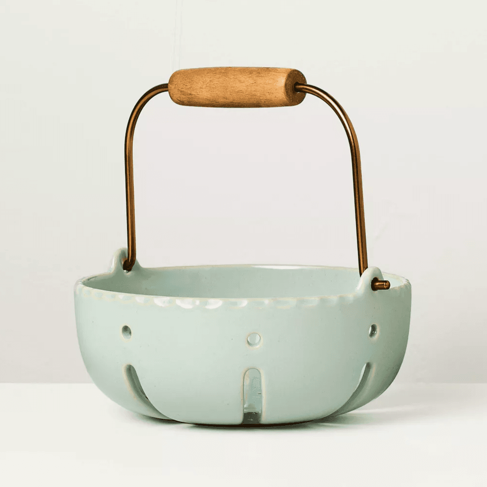 Light green bowl with wooden handle and cutout design on a neutral background.