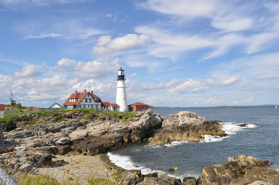 Lighthouse on a rocky coast with a house and blue sky.
