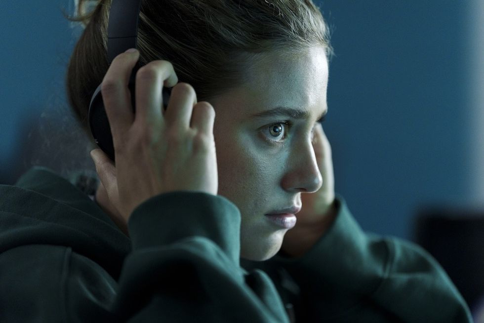 lili reinhart american sweatshop Person intently listening with headphones in a dimly lit room.