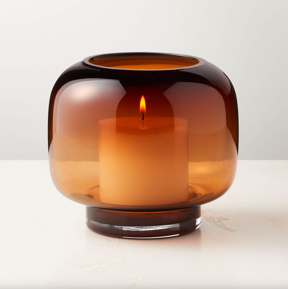 Lit candle in a brown glass holder on a white surface.